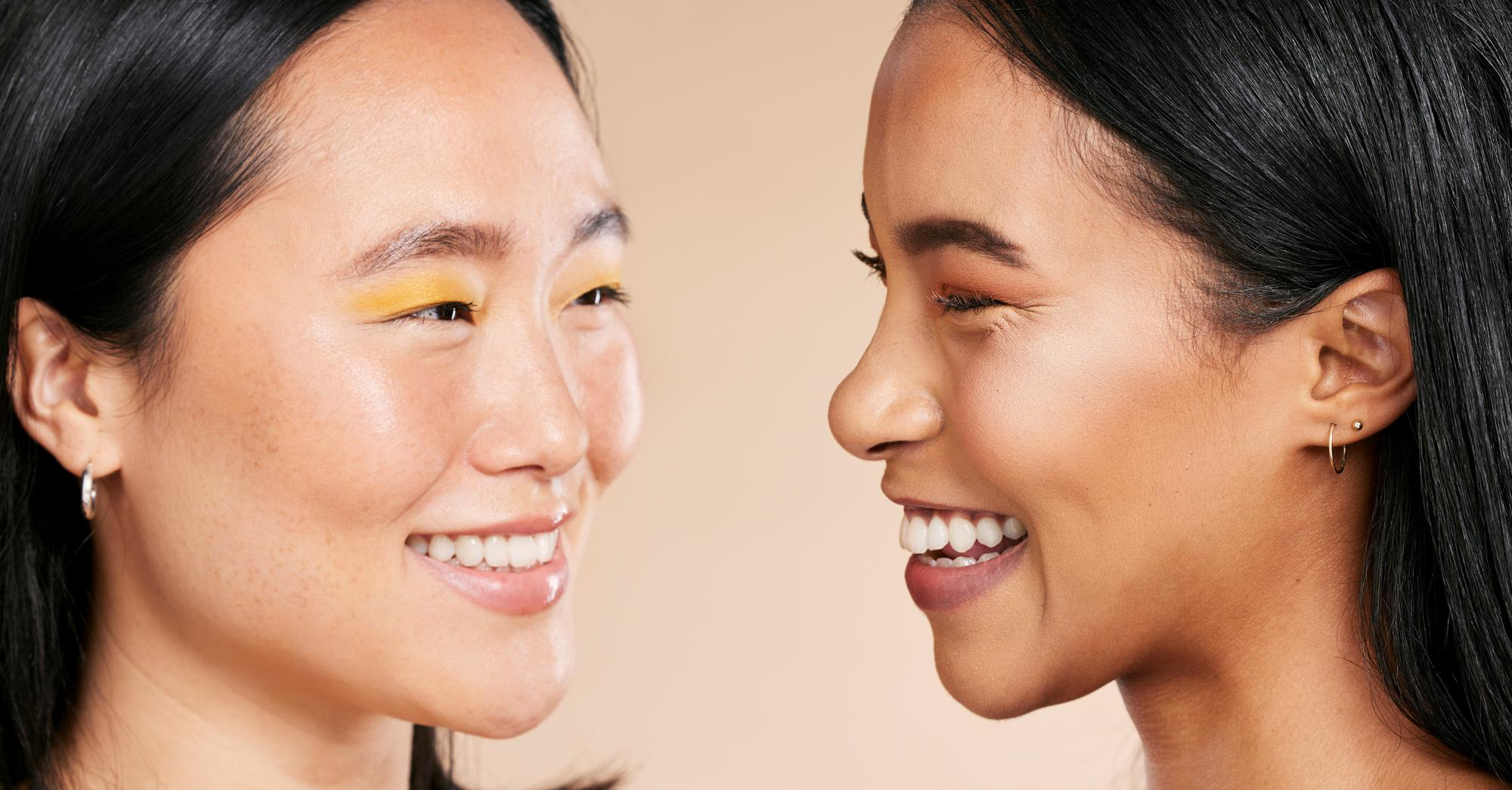 Two smiling women face each other in profile, showing colorful eyeshadow looks
