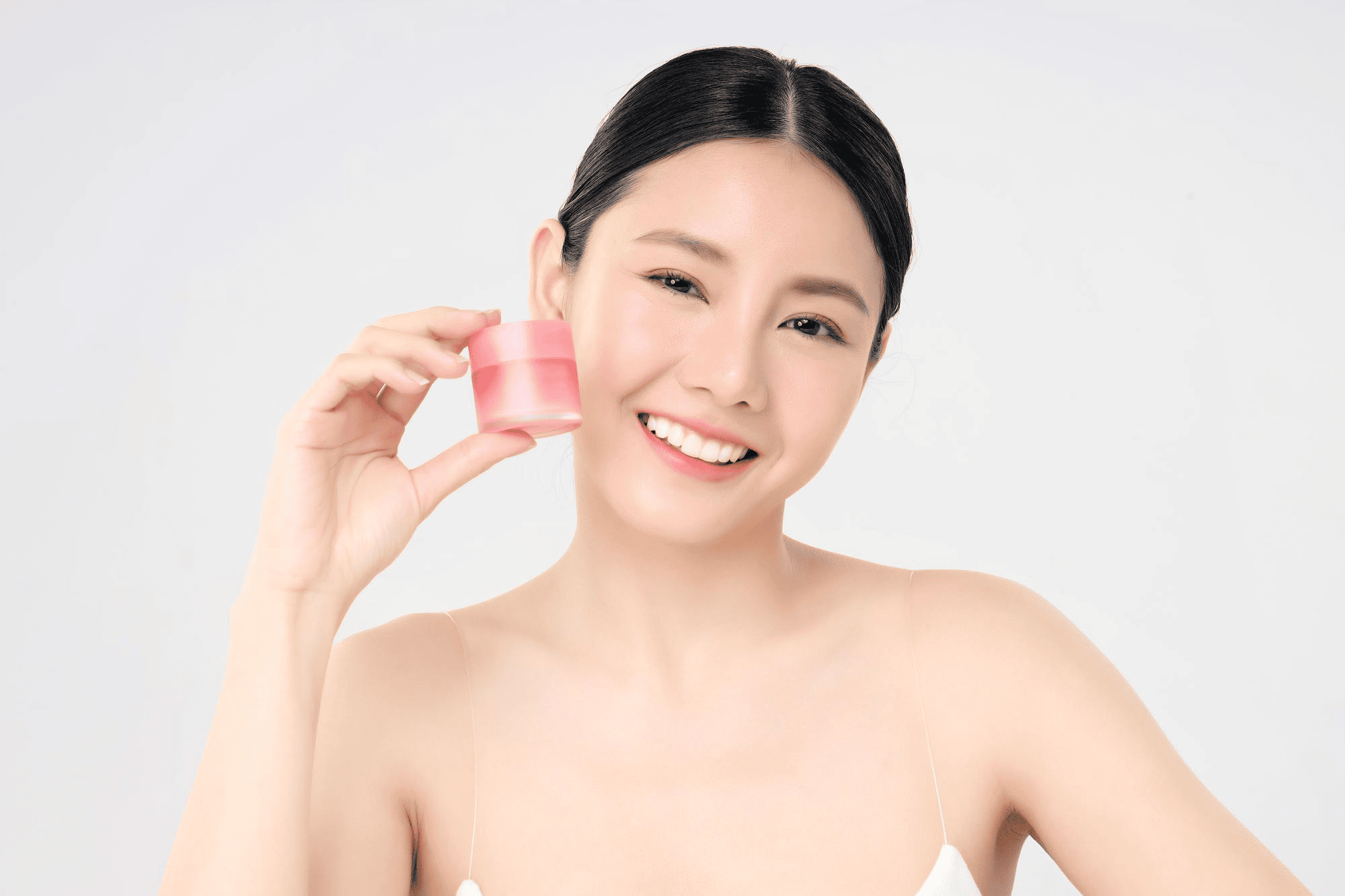 A smiling woman holds up a small pink skincare jar next to her face
