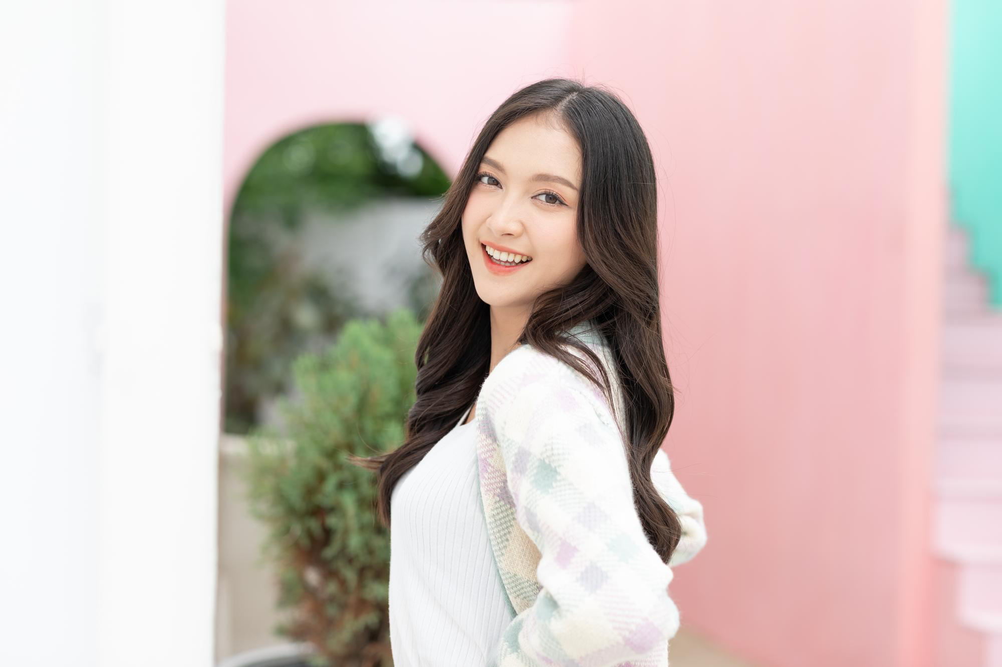 A smiling woman looks back over her shoulder against a pink wall backdrop