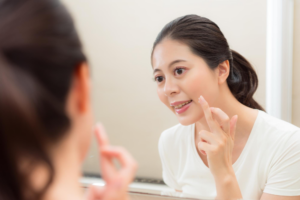 A woman looks at her reflection in a mirror while touching her chin or jawline with her finger