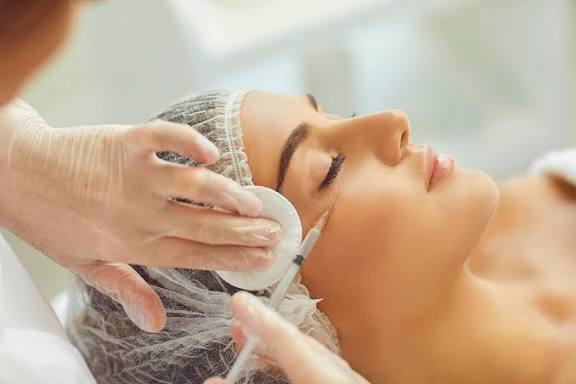 A gloved professional prepares to give a woman a facial injection, wiping the area with a cotton pad