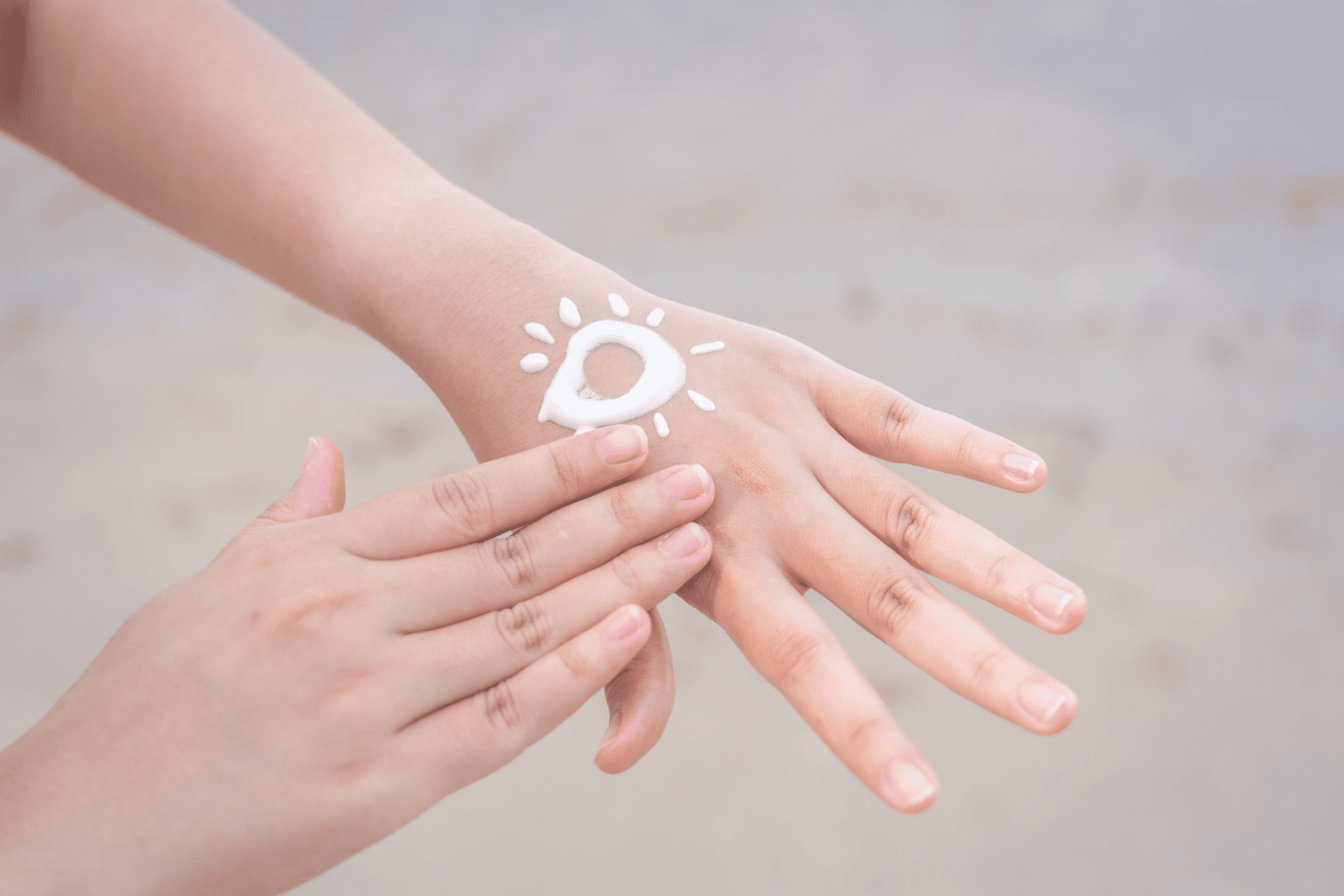 Sunscreen is drawn in a sun shape on the back of a hand, with a finger applying it