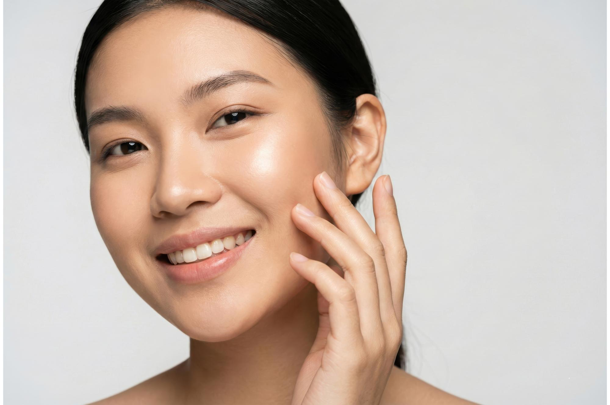 A close-up of a smiling woman touching her cheek, showcasing smooth, glowing skin