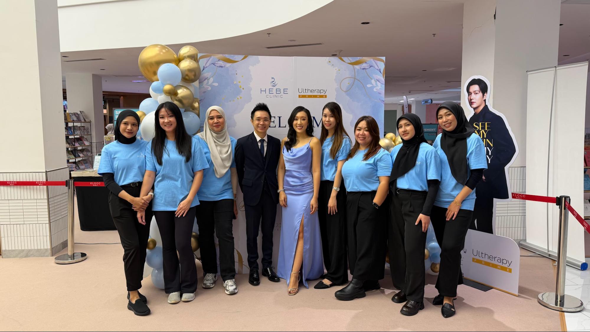 Group photo of the Hebe Clinic KLGCC team posing together in front of a branded event backdrop decorated with gold and blue balloons, celebrating the branch's official opening